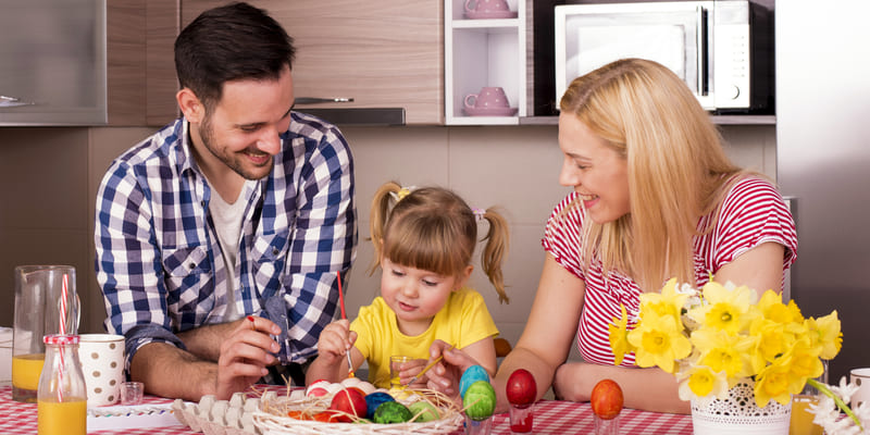 caucasian-family-sitting-kitchen-counter-with-their-daughter-painting-easter-eggs